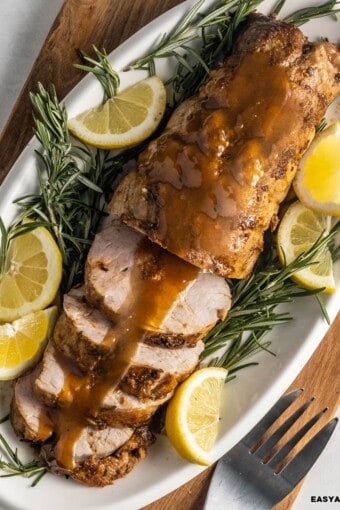 Smithfield pork tenderloin roasted and partially sliced in a platter served with wine sauce, lime wedges, and rosemary sprigs.