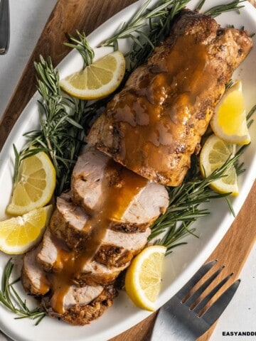 Smithfield pork tenderloin roasted and partially sliced in a platter served with wine sauce, lime wedges, and rosemary sprigs.