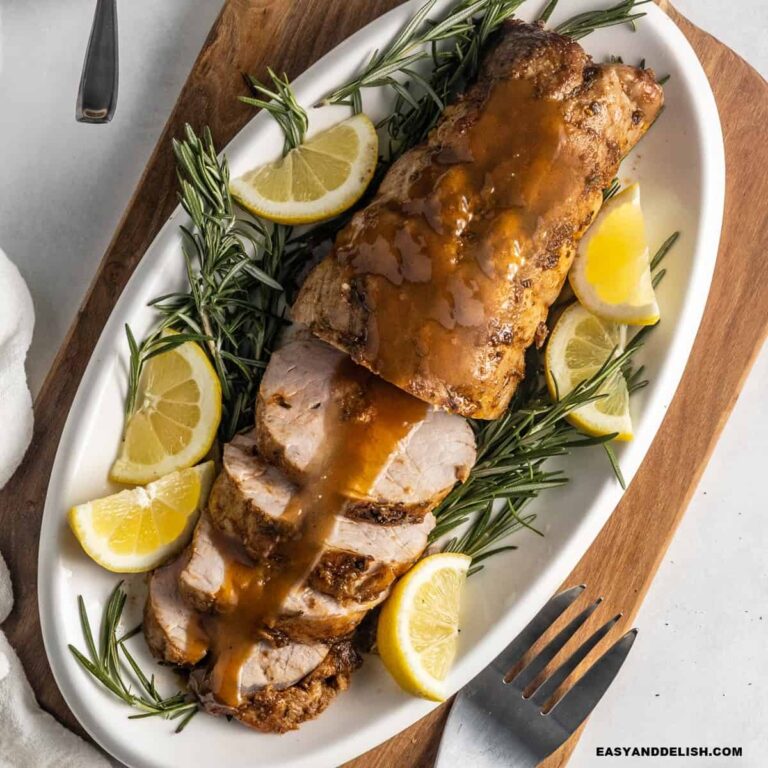 Smithfield pork tenderloin roasted and partially sliced in a platter served with wine sauce, lime wedges, and rosemary sprigs.
