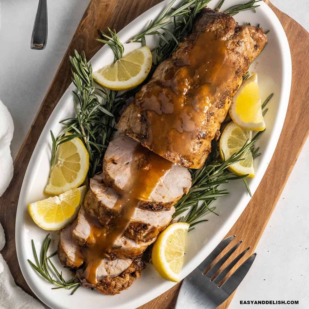 Smithfield pork tenderloin roasted and partially sliced in a platter served with wine sauce, lime wedges, and rosemary sprigs.