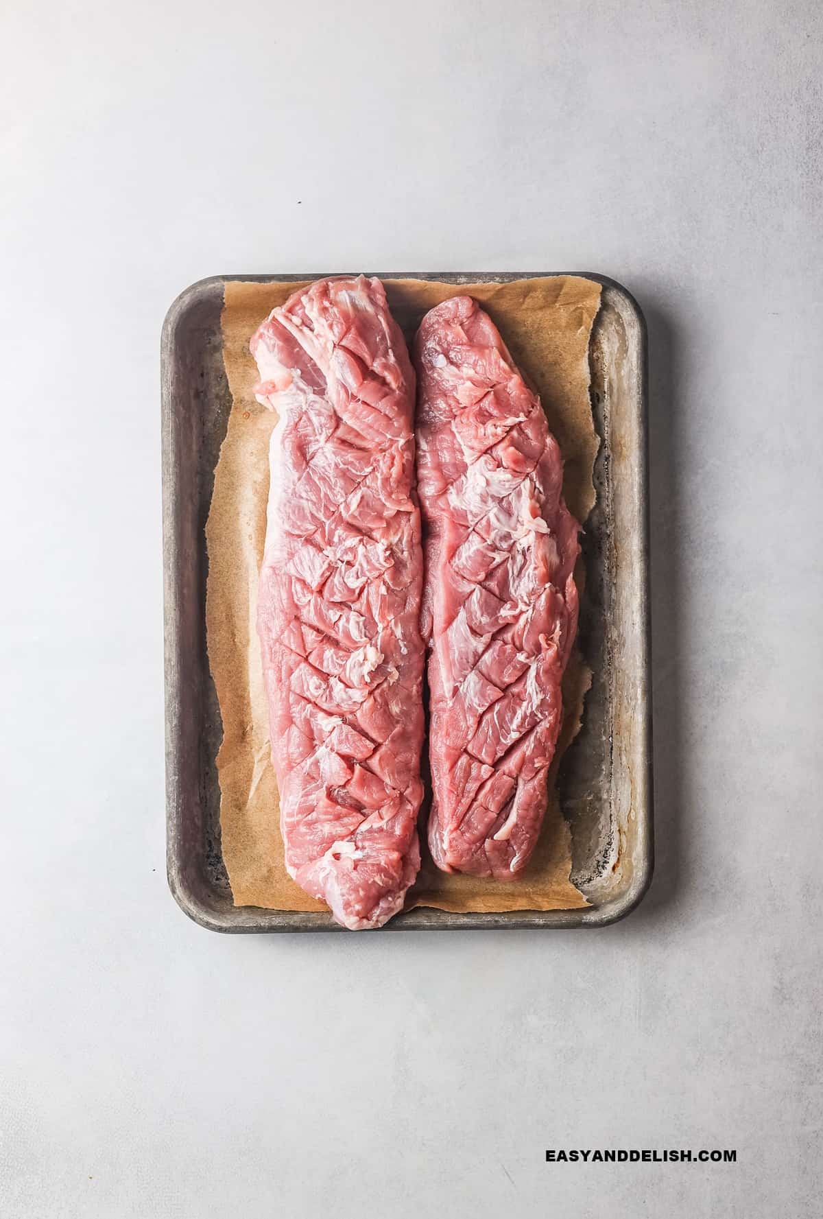 2 pork tenderloins in a baking sheet with their skin scored.