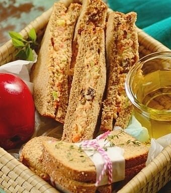 sliced chicken salad sandwiches with a red apple in a basket.