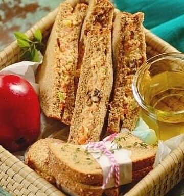 sliced chicken salad sandwiches with a red apple in a basket.