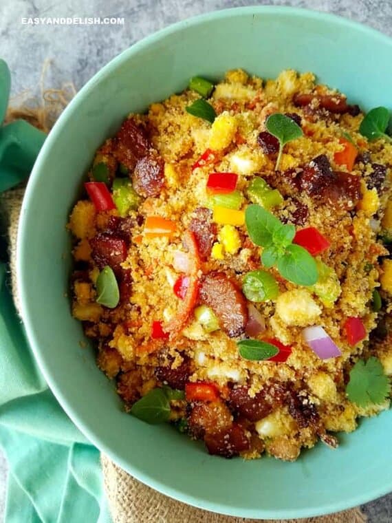 Pastel-green bowl of farofa or toasted seasoned cassava flour, with diced sausage, vegetables, and herbs