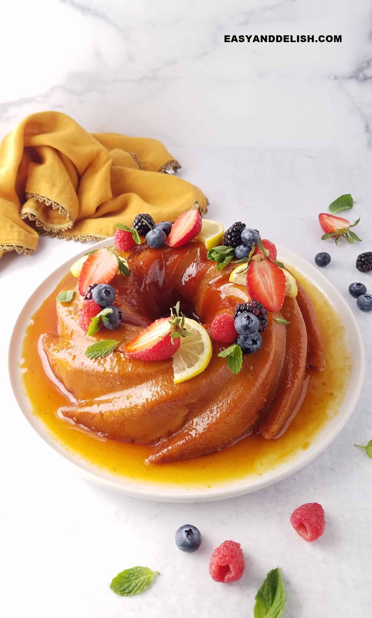 whole caramel bread pudding topped with berries, lemon slcies, and mint leaves in a platter.