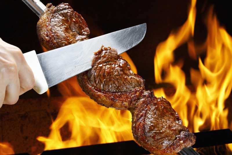 grilled rump cover or culotte steak in long metal skewer close to open flames 