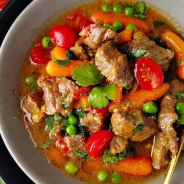 A bowl of Brazilian beef stew or picadinho with red tomatoes, green peas and cilantro, and orange carrots