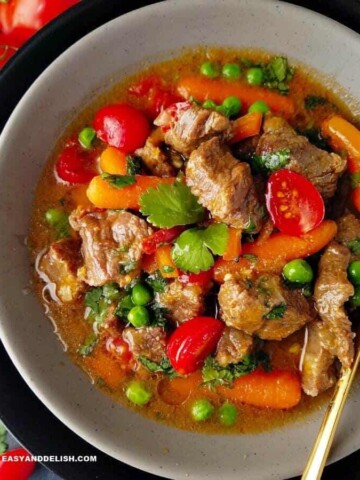 A bowl of Brazilian beef stew or picadinho with red tomatoes, green peas and cilantro, and orange carrots