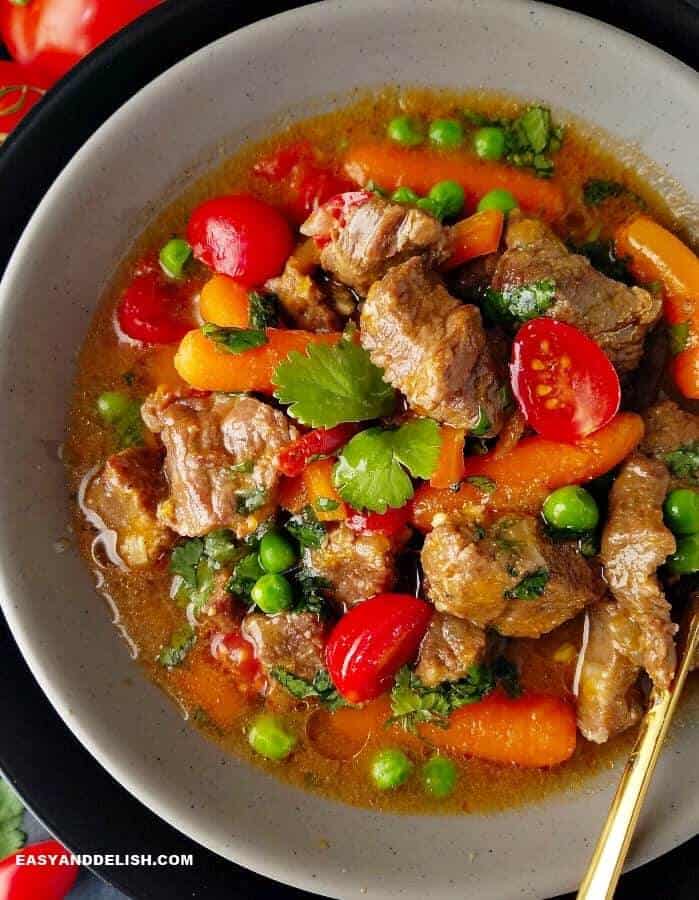 A bowl of Brazilian beef stew or picadinho with red tomatoes, green peas and cilantro, and orange carrots
