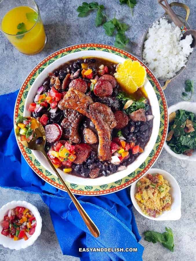 Brazilian black bean and pork stew with sides of white rice, farofa, sauteed collard greens, pico de gallo, and orange caipirinha 