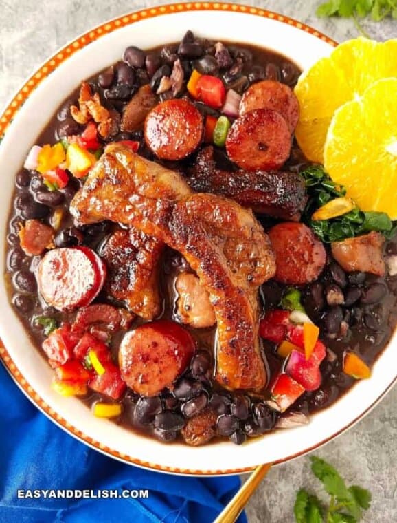 Bowl of feijoada black bean stew with pork sausage, pork ribs, oranges and collard greens