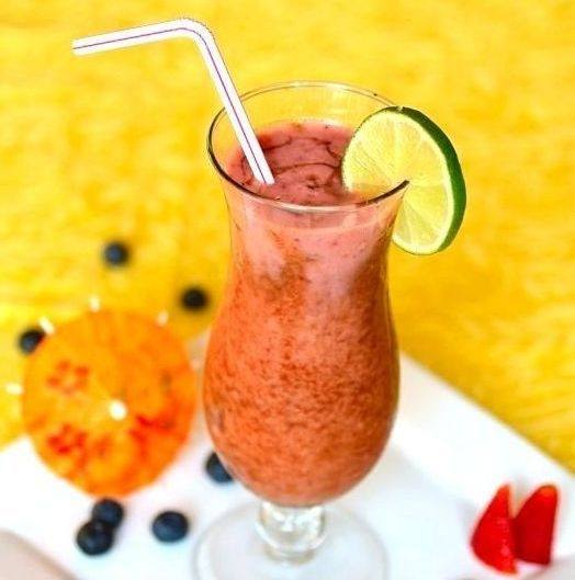 Rosy red tropical fruit cocktail drink in a clear cocktail glass, with a straw, and garnished with a slice of lime