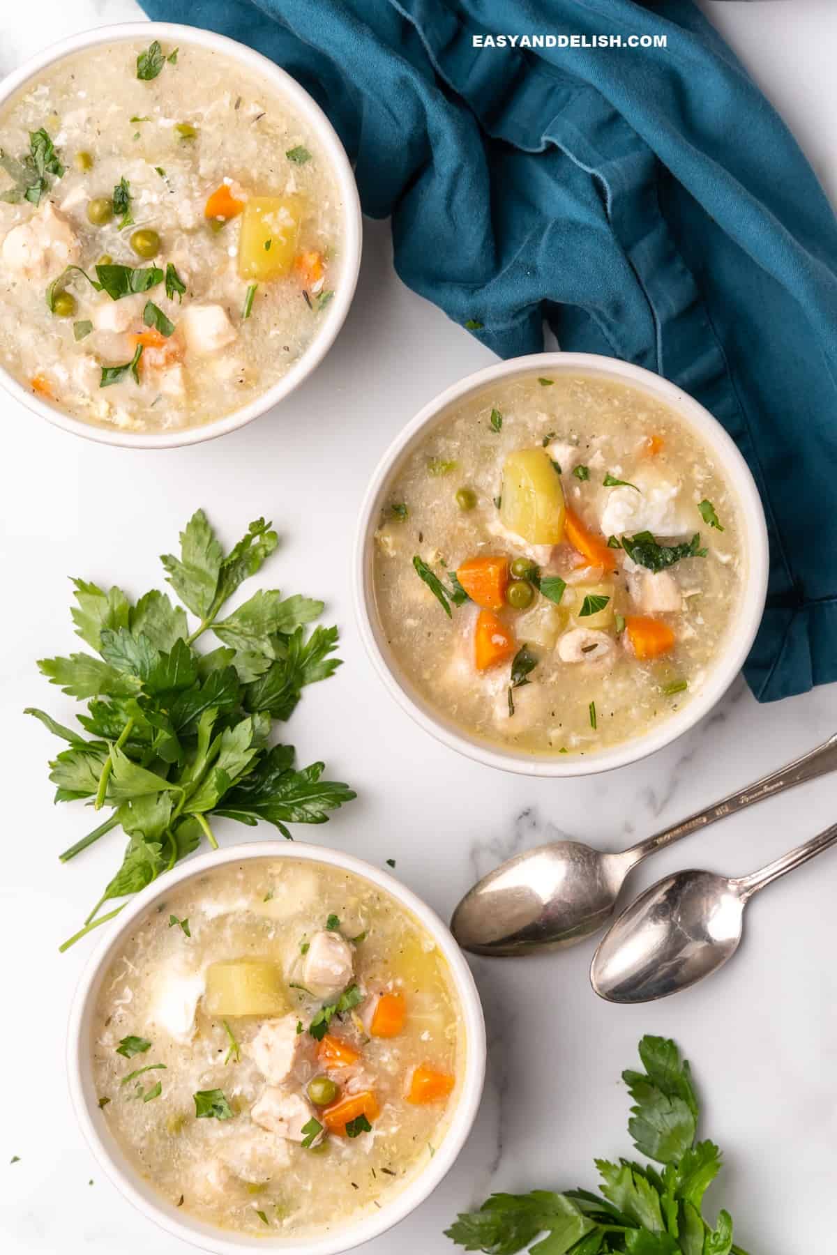 3 bowls of easy chicken and rice soup with herbs and spoons on the side