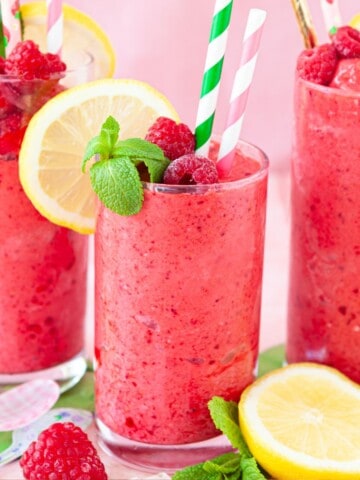 Three glasses of fruit cocktail drink garnished with mint leaves, raspberries and lemon slices.