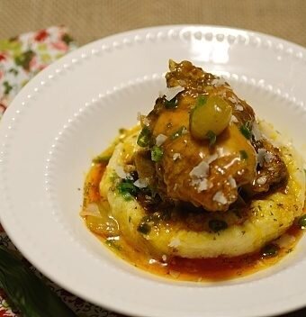 A slice of polenta topped with chicken stew in a white bowl