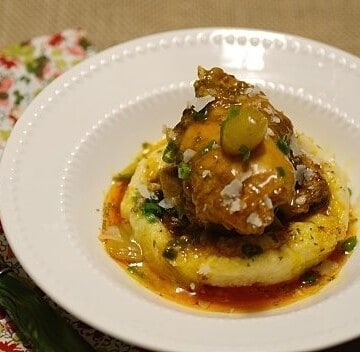 A slice of polenta topped with chicken stew in a white bowl