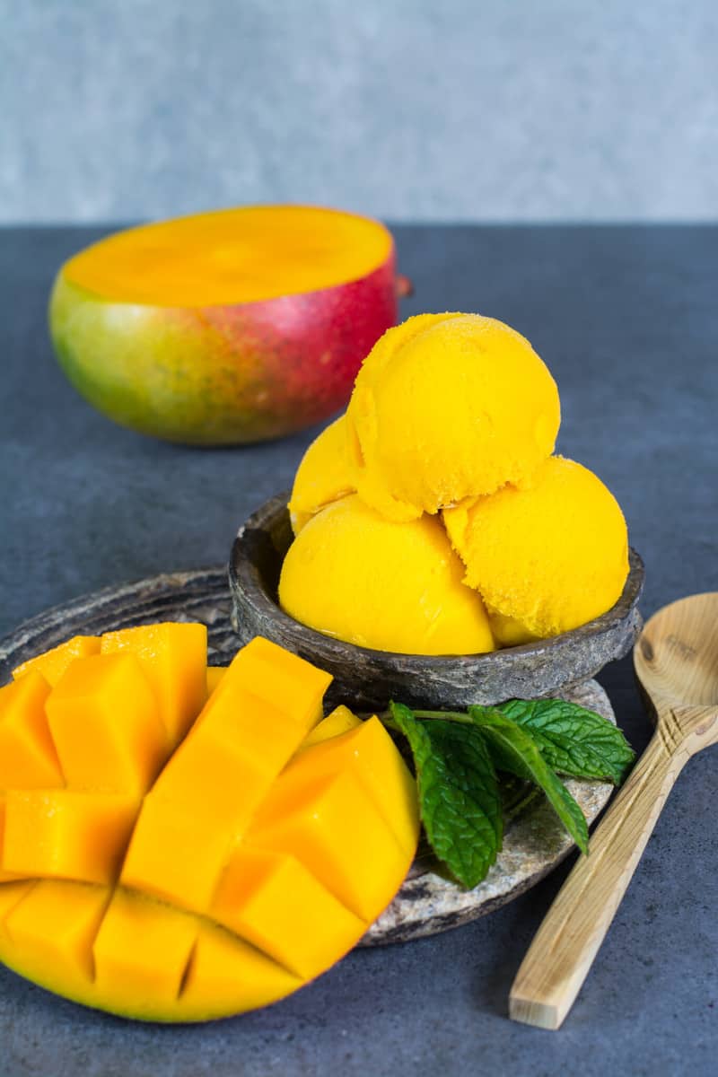 Scoops of mango ice cream with condensed milk piled up in a bowl and garnished with fresh mint leaves.