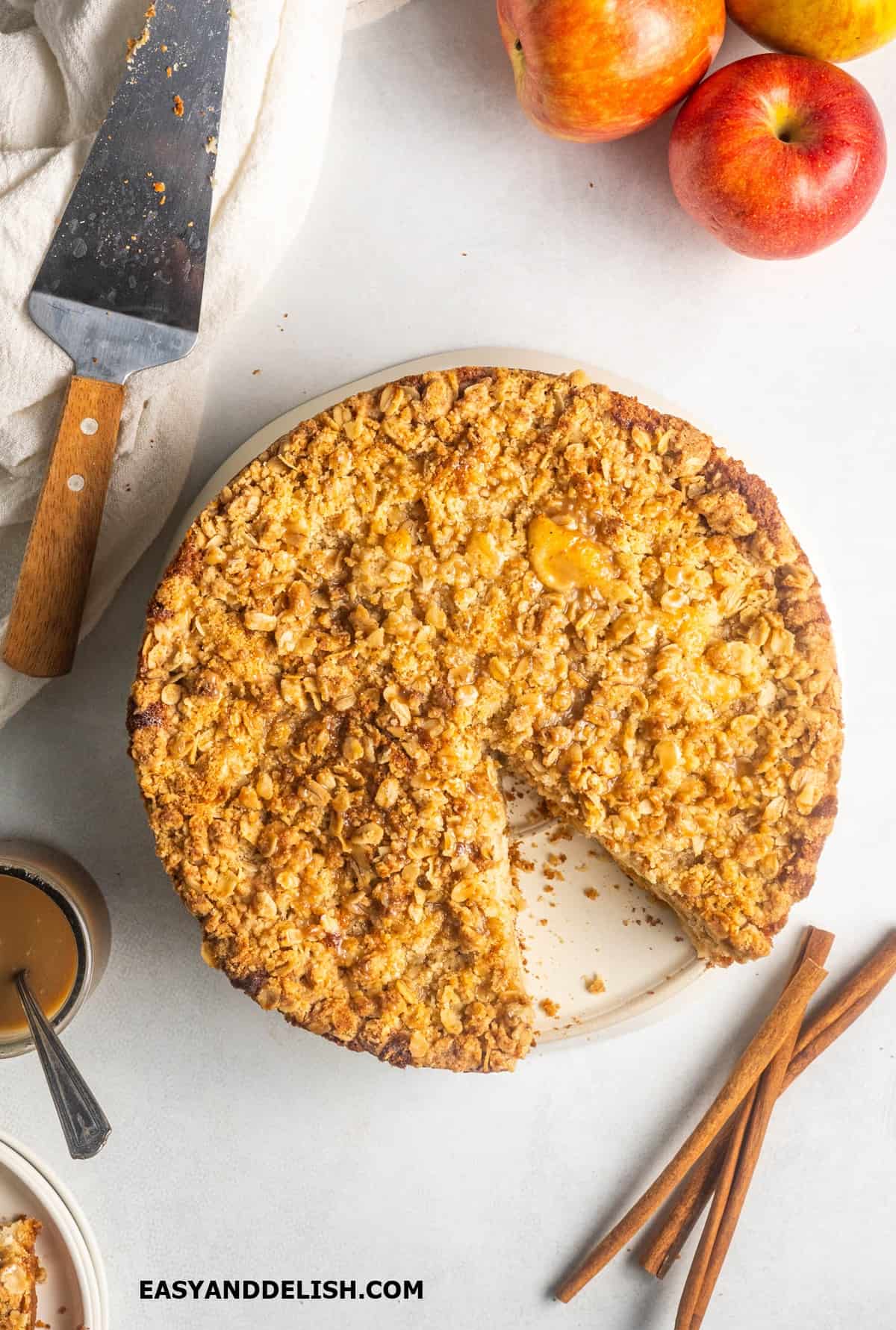 apple streusel cake wwith caramel in a platter , partially sliced with some ingredients around it. 