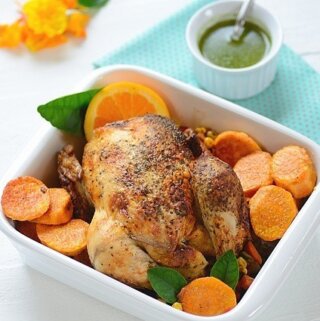A baking dish with roast chicken with veggies and a bowl of chimichurri on the side