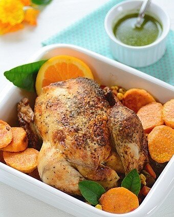 A baking dish with roast chicken with veggies and a bowl of chimichurri on the side