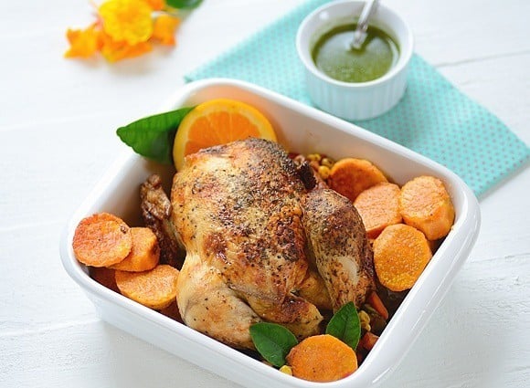 A baking dish with roast chicken with veggies and a bowl of chimichurri on the side