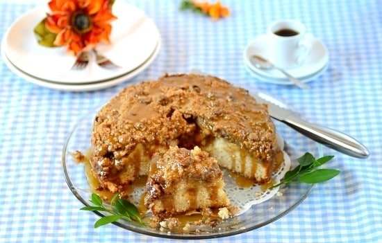 A plate with apple streusel cake partially sliced and a cup of coffee on the background 