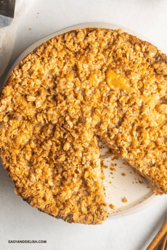 caramel apple cake with streusel topping partially sliced in a plate.