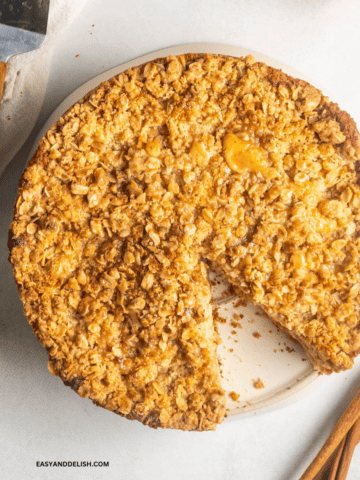 caramel apple cake with streusel topping partially sliced in a plate.