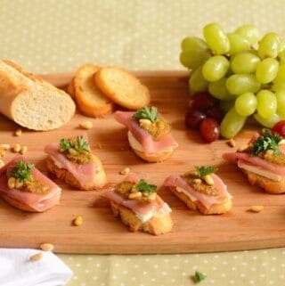 crostini with cheese on a serving board with green grapes