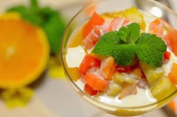 Wine glass filled with salada de frutas or fruit salad, drizzled with whipping cream and garnished with mint leaves