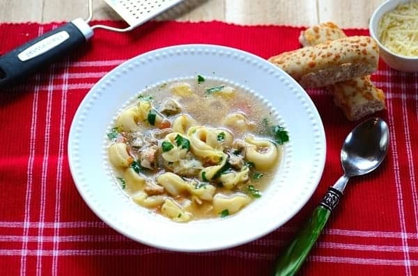 A bowl of tortellini soup with bread on the side
