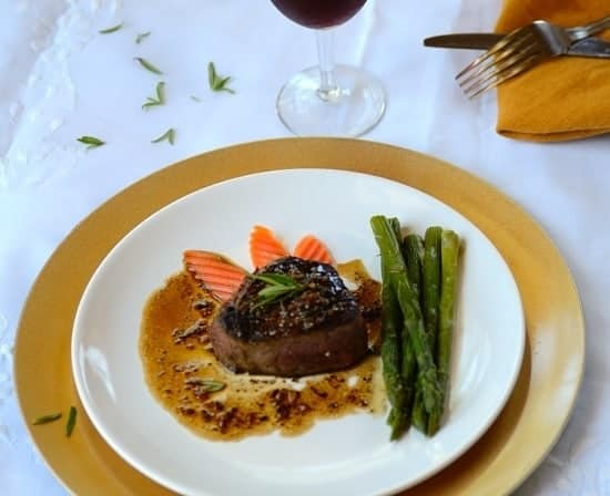 A plate with filet mignon with veggies and garnishes on the sides