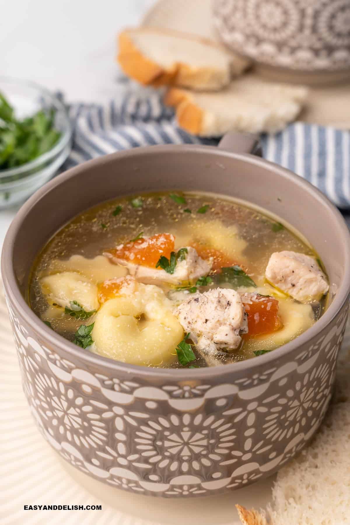 a bowl of tortellini in brodo with slices of bread on the background