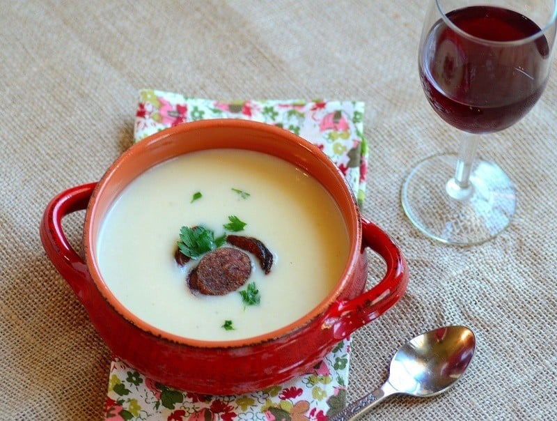 A bowl of soup sitting on a table with a glass of wine on the side