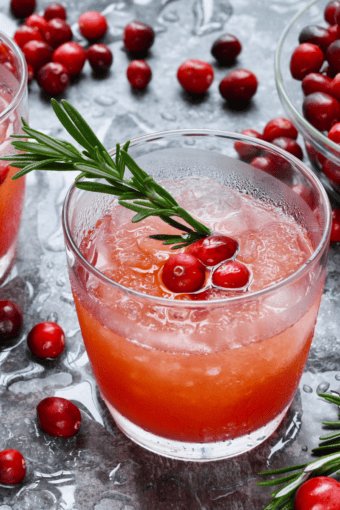 a glass of sparkling cranberry cocktail with vodka plus some fresh cranberries and rosemary sprigs.
