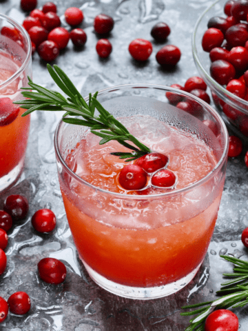 a glass of sparkling cranberry cocktail with vodka plus some fresh cranberries and rosemary sprigs.