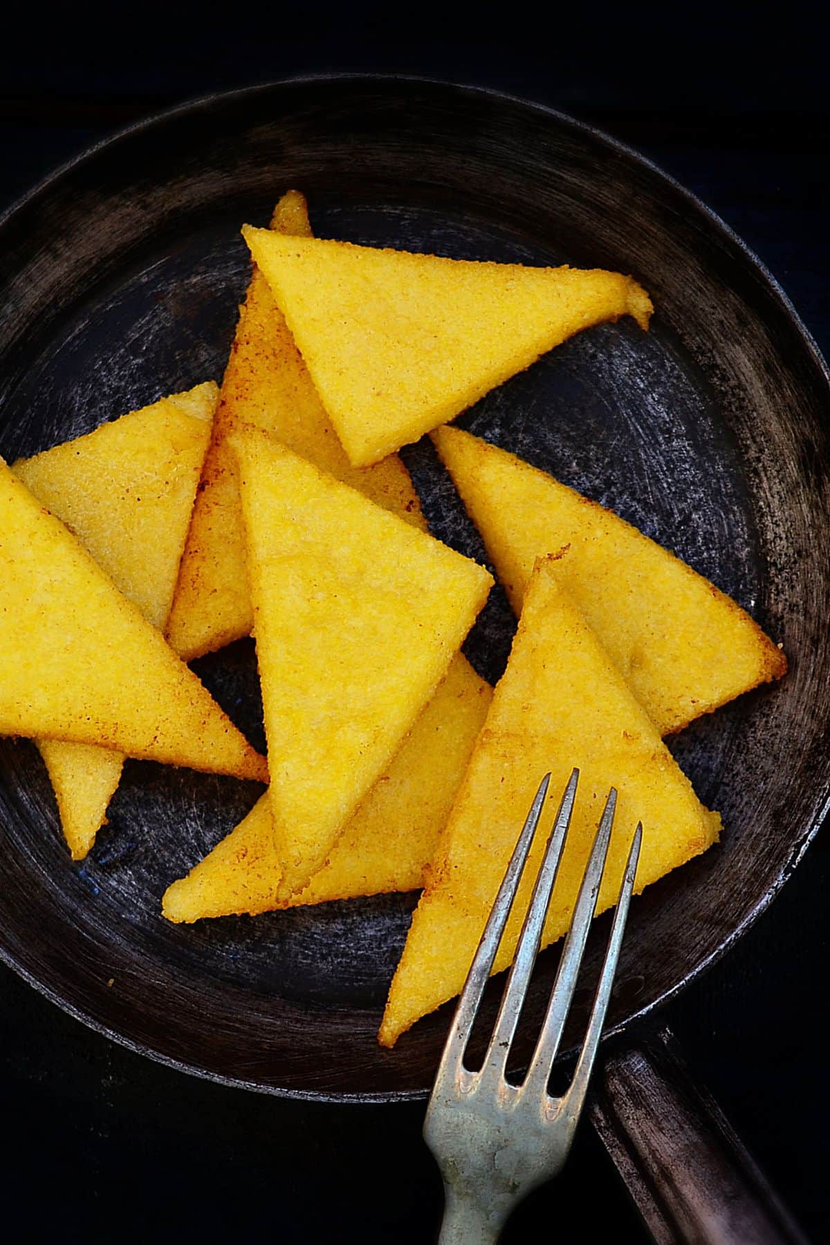 Triangle-shaped fried poleta cakes in a skillet. 