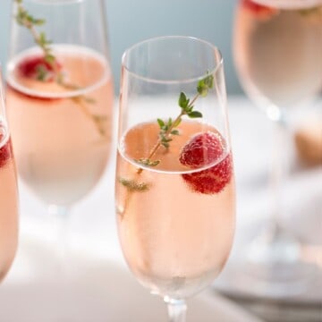 Vodka champagne cocktail garnished with thyme and raspberry in flute glasses.