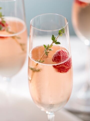Vodka champagne cocktail garnished with thyme and raspberry in flute glasses.