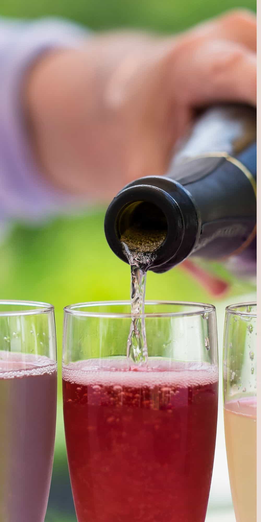 A hand pouring prosecco into a glass with a mixture of liquids. 