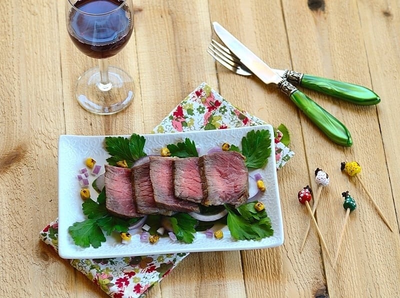a platter with sliced carne de sol (beef) and a glass of wine plus cutlery