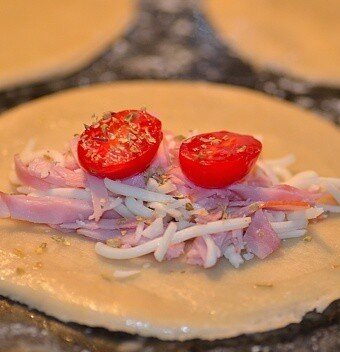 ham, cheese, tomato, and oregano filling on top of a disc of empanada dough