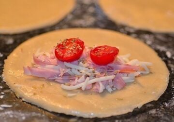 ham, cheese, tomato, and oregano filling on top of a disc of empanada dough