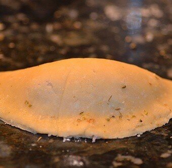 a filled disc of empanada dough folded shut into a half moon shape with the edges sealed