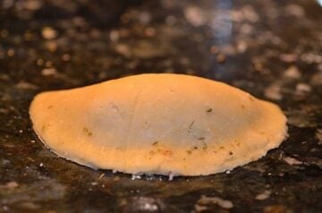a filled disc of empanada dough folded shut into a half moon shape with the edges sealed