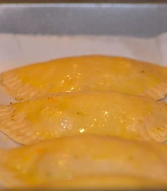 filled and sealed empanada disc with the edges crimpled and brushed with egg yolk