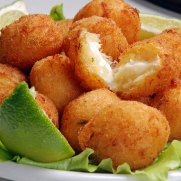 a bunch of cod cakes in a tray with lime wedges
