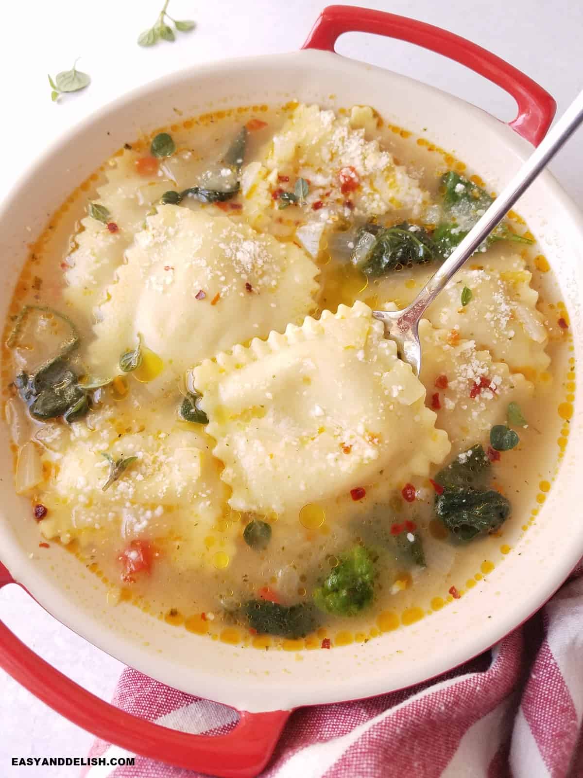 a spoon held over a bowl of ravioli in broth.