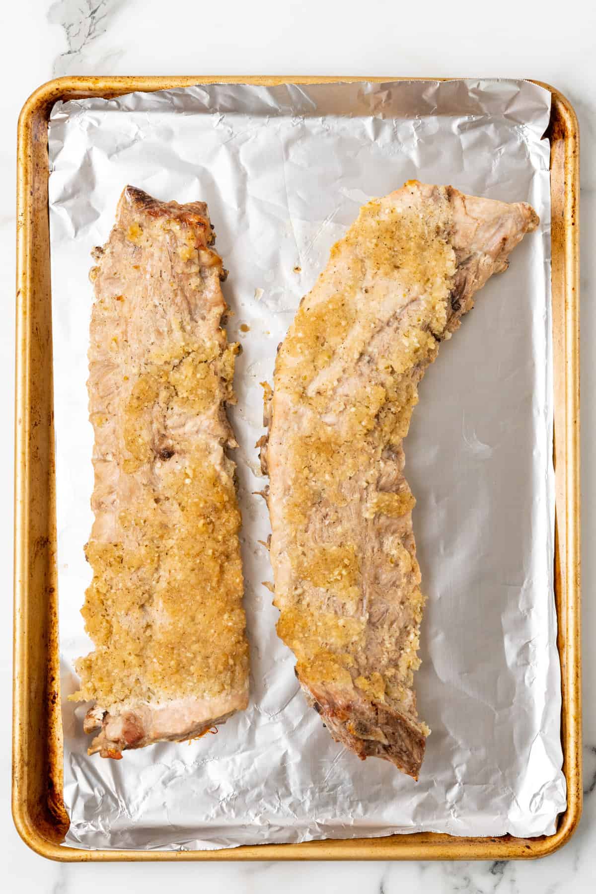 two whole racks of baked pork ribs in  a baking sheet.