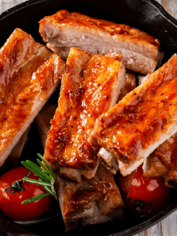 oven baked pork ribs served in a skillet with some veggies.